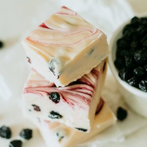 blueberry and cream fudge stacked next to a bowl of blueberries