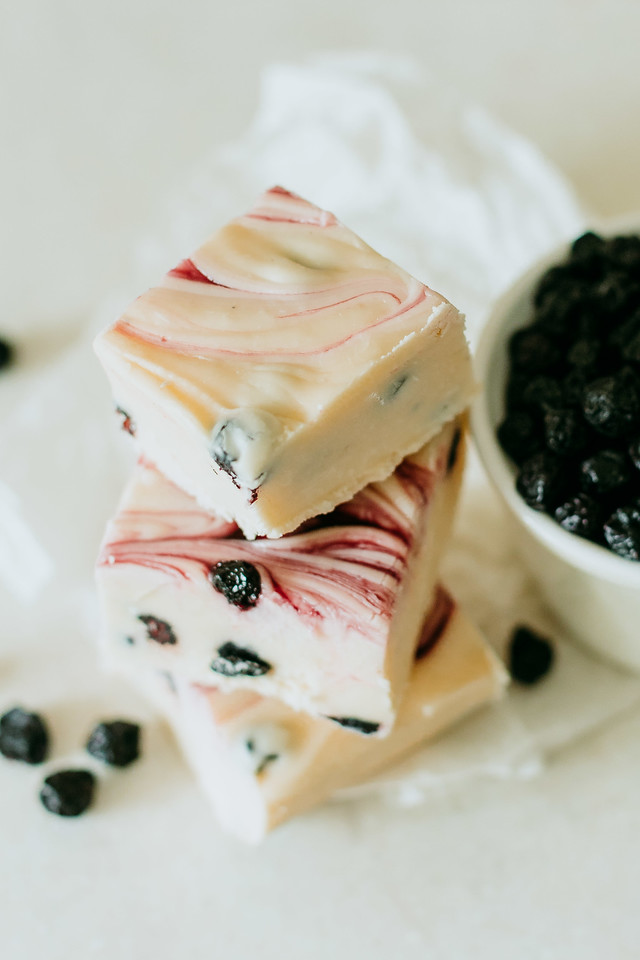 blueberry and cream fudge stacked next to a bowl of blueberries